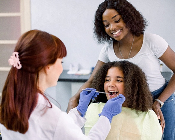 A dentist checking a young girl’s smile to determine if she needs a dental crown in Coppell