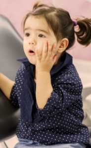 Little girl in need of kids' dental emergency treatment holding cheek in pain