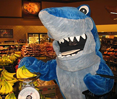 Shark Mascot purchasing bananas at grocery store