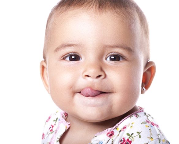 A baby wearing a floral top and sticking its tongue out after seeing a lip and tongue tie dentist in Coppell, TX