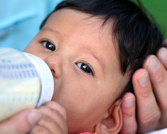 An individual cradling a baby while trying to feed them a bottle