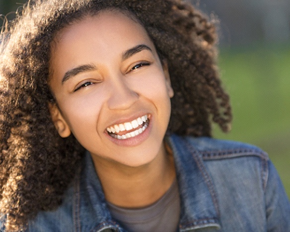 A teenage female wearing a denim jacket and smiling while outside