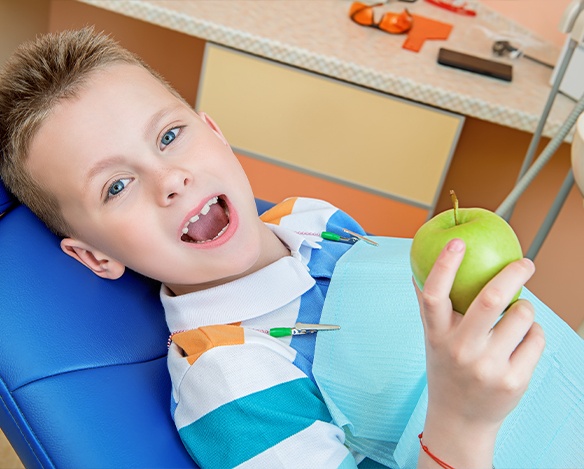 Child in dental chair for preventive dentistry holding a green apple