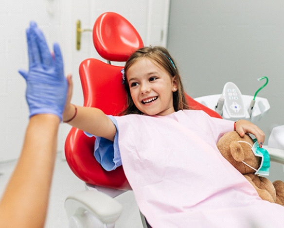A little girl holding a teddy bear and giving her dentist a high-five before having pulp therapy performed