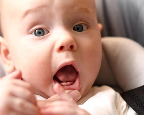 A little baby lying on its back while an adult exposes two erupting bottom teeth