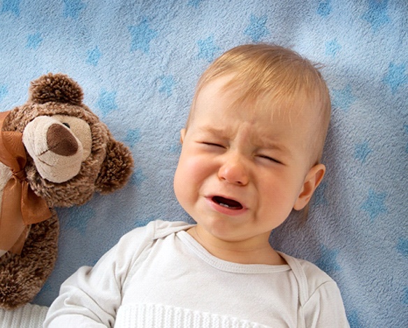 A baby crying while lying on its back with a stuffed teddy baby nearby