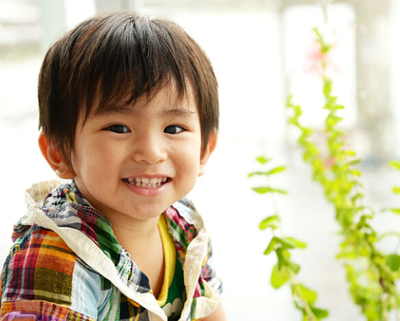 A little boy wearing a plaid jacket and smiling, showing off his healthy teeth