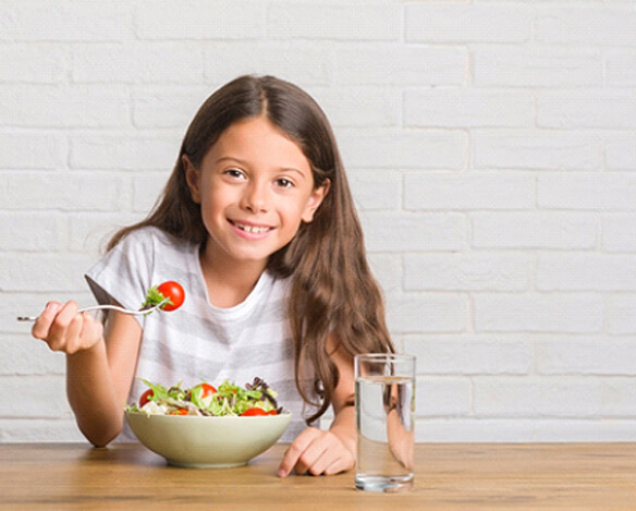 A young girl sitting at a table and eating a salad full of healthy vegetables
