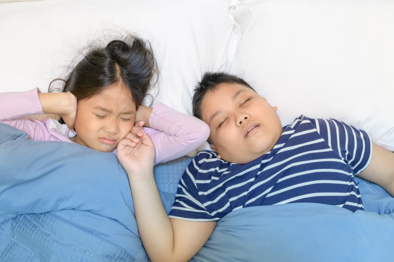 a young boy asleep with his mouth open and a young girl covering her ears because of his snoring 
