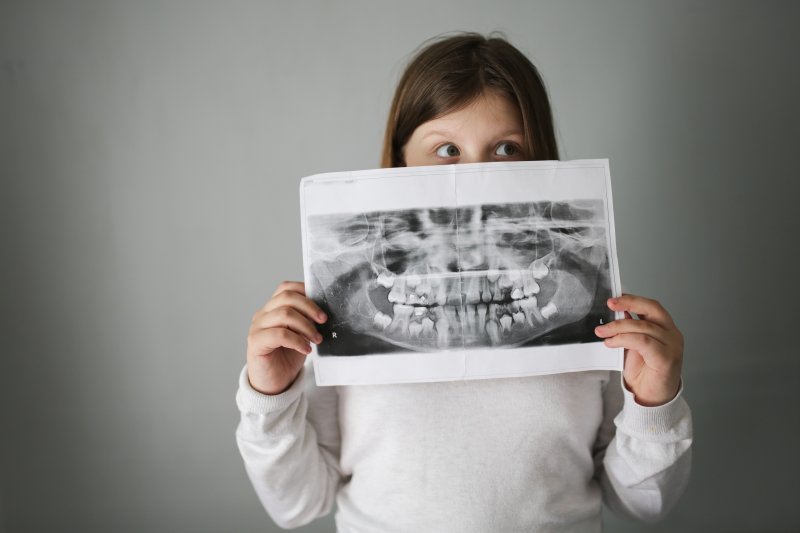 a little girl holding up a dental x-ray in front of her mouth and nose