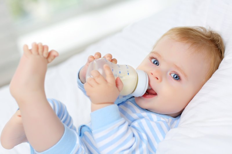 a baby holding a bottle filled with formula and lying on its back