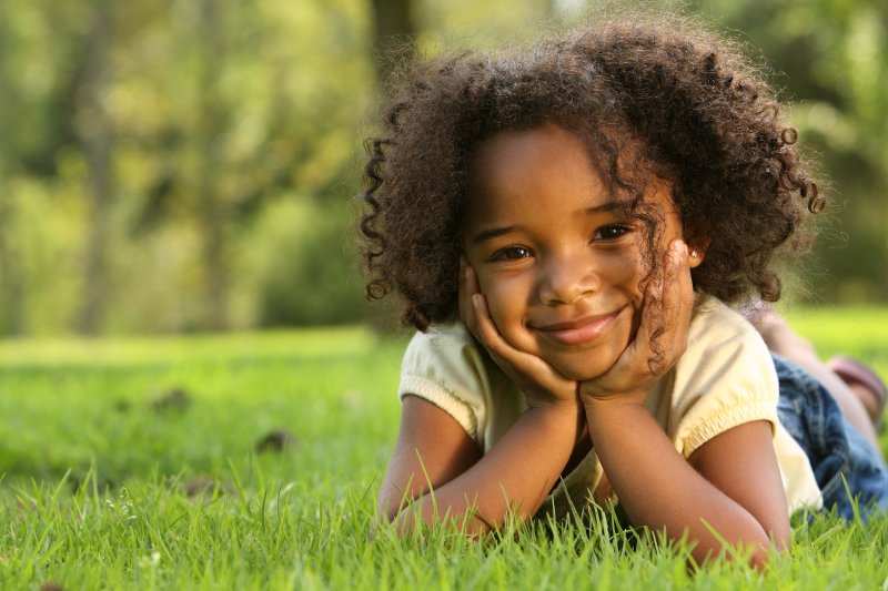 a little girl laying in the grass and holding her face between her hands while smiling