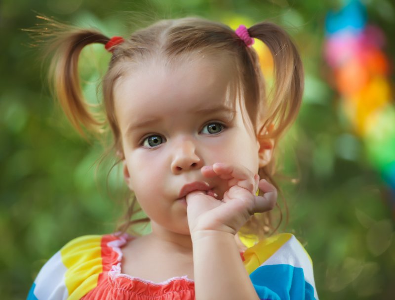 a toddler with pigtails and a colorful dress sucks her thumb