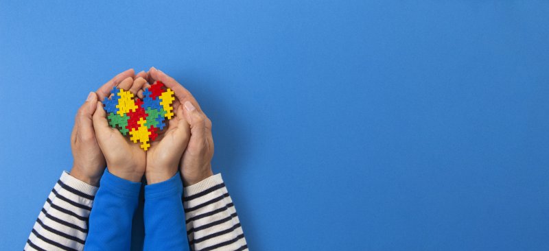 a colorful heart puzzle inside a child’s hands that are surrounded by an adult’s hands