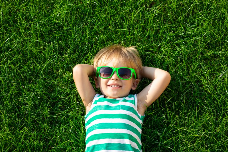 a child laying in the grass while wearing sunglasses